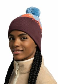 Gorro de lana en color burdeos con un pompón azul. Presenta un patrón montañoso en naranja y azul. Textura suave, ajuste ceñido.