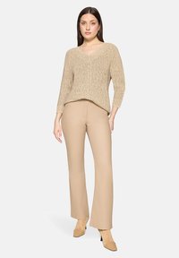 Pull beige en tricot avec col en V, manches trois-quarts, associé à un pantalon évasé beige clair et des bottines assorties.