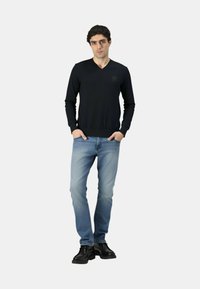 Maglione nero a maglia con scollo a V, jeans azzurri e stivali neri. Il maglione presenta un logo discreto, con polsini e orlo a coste.
