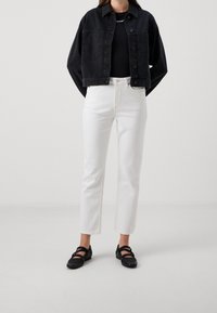 Chaqueta de mezclilla negra, pantalones blancos de talle alto y zapatos planos negros. La chaqueta tiene dos bolsillos y un cierre de botones.