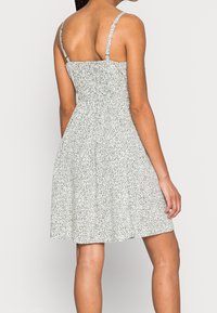 Mujer vestida con un vestido sin mangas, de longitud hasta la rodilla, con un pequeño estampado de flores verdes y blancas, vista desde atrás con el cabello trenzado.