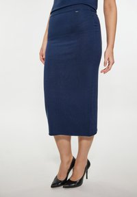 Knielanger marineblauer Bleistiftrock aus geripptem Material. Verfügt über eine figurnahe Silhouette mit einem glatten Bund und einem kleinen Metallemblem.
