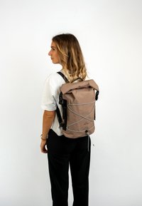 Barna vízálló, felgöngyölhető hátizsák szürke gumis részlettel, fekete pántokkal és logóval. Sima felület, téglalap alak, minimalista dizájn.