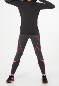 Schwarzes Langarmoberteil mit Kapuze, kombiniert mit grauen Leggings, die pinke geometrische Akzente aufweisen; beide aus dehnbarem Sportstoff gefertigt.