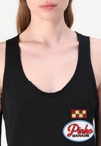 Μαύρο αμάνικο μπλουζάκι με στρογγυλή λαιμόκοψη και δύο κεντητές ρέπλικες: ένα τετράγωνο σχέδιο σε κόκκινο και κίτρινο, και μια μπλε ωοειδής ετικέτα με την ένδειξη "Pinko Garage."