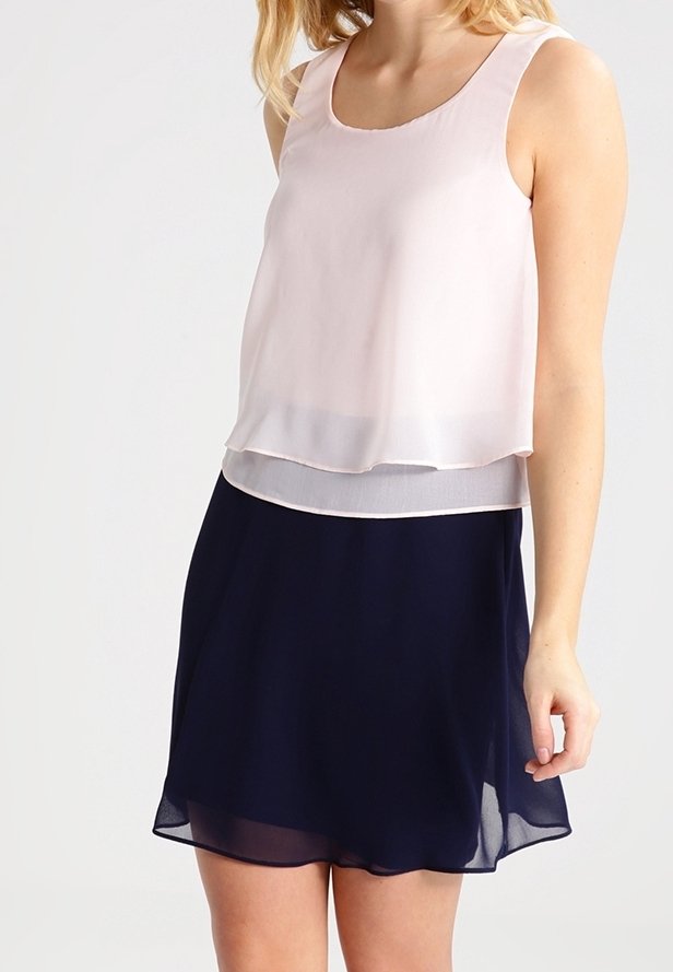 Top bez rukávů s lehkým růžovým průsvitným přehozem a tmavě modrou sukní. Materiál je hladký s plynulým drapováním, což vytváří vrstvený efekt.
