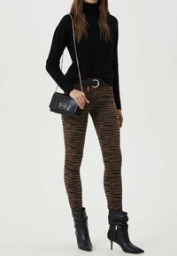 Jeans ajustados a rayas de cebra en tonos marrón y negro, combinados con un suéter de cuello alto negro, un bolso texturizado negro y botas de tacón stiletto negras.