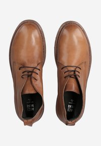 Chaussures montantes en cuir marron avec une finition lisse, bout rond, fermeture à lacets et semelle texturée. Doublure intérieure noire et marque visibles à l'intérieur.