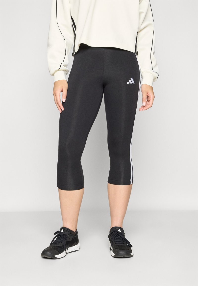 Juodos trumpintos leggingai, pagaminti iš tamprios medžiagos, su baltais šoninėmis juostelėmis ir „Adidas“ logotipu kairiajame šlaunyje.