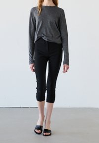 Szary długi rękaw z luźnym krojem, połączony z czarnymi dopasowanymi spodenkami capri oraz czarnymi klapkami. Prosty fason, gładka faktura.
