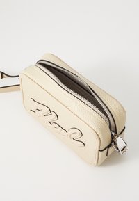 Borsa a tracolla in pelle crema con testo impresso, bordi neri a contrasto, chiusura con zip superiore e dettagli in metallo argentato. Forma rettangolare.