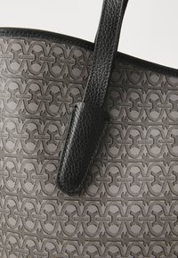 Grey patterned tote bag featuring a textured surface, black leather accents, and dual handles for carrying convenience.