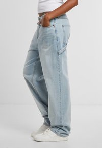 Himlenblå denimjeans med en lös passform, som har sidofickor och en slät yta, kombinerade med vita sneakers för kontrast.