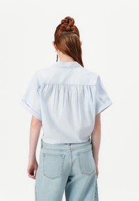 Camisa de manga curta branca e azul riscada com um design de costas pregueadas, combinada com umas calças de ganga de cintura alta azul claro.