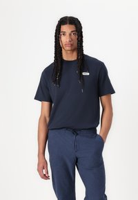 Navy blue short-sleeve t-shirt with a crew neck and a small logo patch. Paired with relaxed-fit navy blue pants with drawstring waist.