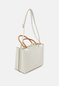 Sac fourre-tout tissé blanc avec des poignées tressées couleur fauve. Présente une forme structurée, des accents dorés et une bordure noire contrastante.