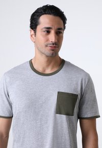 T-shirt grigia a maniche corte in cotone, con tasca e rifiniture in verde oliva. Tessuto liscio con un design casual.
