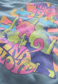 Felpa blu con una vivace stampa grafica caratterizzata da forme e motivi multicolori, inclusi un maialino rosa e testo stilizzato.