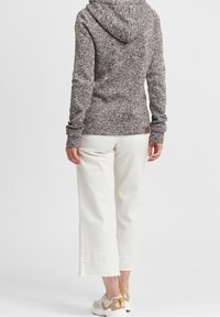 Felpa a cappuccio marrone maculato con cappuccio spazioso, maniche lunghe e tessuto testurizzato; abbinata a pantaloni bianchi a gamba larga e sneakers beige.