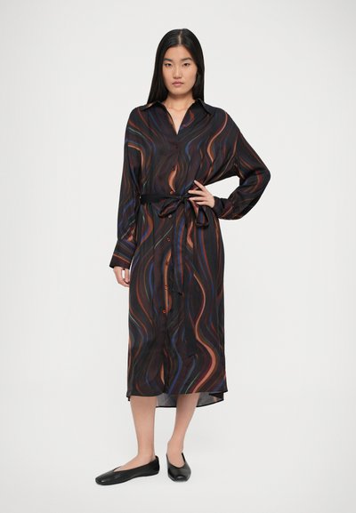 Abito nero con bottoni, con motivi multicolori ondulati, maniche lunghe e cintura legata in vita. Tessuto morbido con lunghezza sotto il ginocchio. Scarpe flat nere.