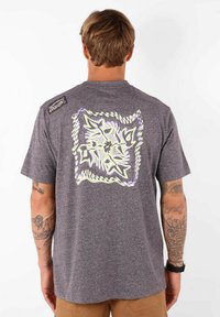 T-shirt gris à manches courtes avec un grand motif graphique multicolore au dos, en tissu texturé légèrement chiné.