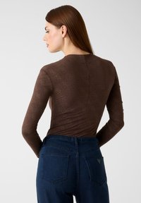 Bruin top met lange mouwen en subtiel diamantpatroon, met een gladde textuur. Gecombineerd met high-waisted donkerblauwe jeans met achterzakken.