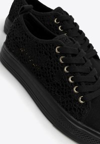 Zapatillas negras con cordones, con unUpper de punto texturizado, que presentan ojales dorados, una suela de goma negra gruesa y un diseño sin costuras.