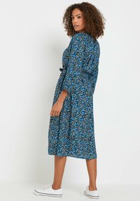Vestido midi azul con estampado floral, de mangas largas, con cintura ceñida y una falda fluida. Combinado con zapatillas blancas para un look informal. Textura suave.