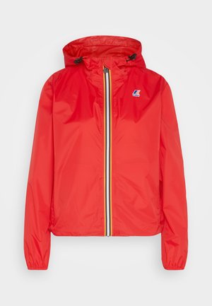 Giacca leggera rossa con cappuccio, dotata di zip frontale completa con striscia gialla e nera, polsini elastici e un piccolo logo sul petto.