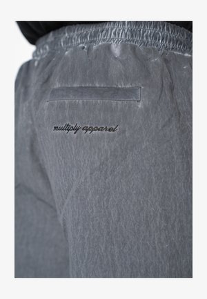 Close-up of gray fabric pants with elastic waistband and back pocket above black embroidered "multiply apparel" text.