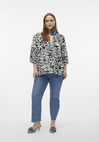 Black and white zebra-print top with a V-neck, three-quarter sleeves, paired with light blue straight-leg jeans and coordinating blue heeled sandals.