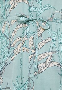 Vaaleansininen kangas, jossa on beige ja tummansininen lehtikuvio, jossa on napit keskellä ja sidottava kangasvyö vyötäröllä.