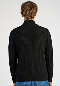 Schwarzer Strickpullover mit strukturiertem Rippenmuster, hohem Kragen und eng anliegenden Bündchen. Die Rückansicht zeigt ein sauberes, stromlinienförmiges Design.