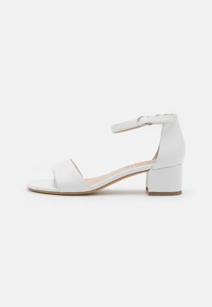 Sandale blanche à petit talon avec bride de cheville et boucle, bout ouvert, talon bloc, vue de l’intérieur sur fond blanc.