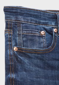 Bolsillo de jeans de mezclilla azul oscuro con remaches de cobre y detalle de costura naranja en la textura de la tela.