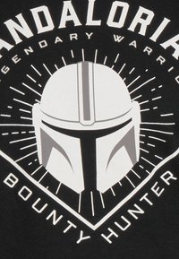 Zwarte t-shirt met witte grafische ontwerpen van een helm in het midden, omringd door zonnestralen en de tekst "MANDALORIAN BOUNTY HUNTER."