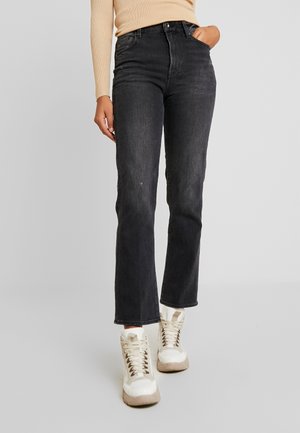 Jeans de mezclilla negra con corte recto, cintura alta y ligeros detalles de desgaste. Combinados con zapatillas blancas con acentos beiges.