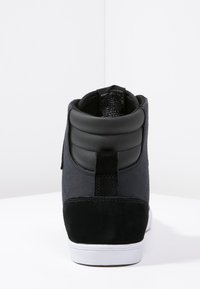 Black high-top sneaker with a textured fabric upper, smooth leather accents, padded collar, and contrasting white rubber sole.