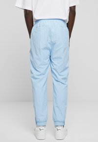 Light blue, lightweight trousers with an elastic waistband and gathered cuffs, featuring a smooth texture and two rear pockets.
