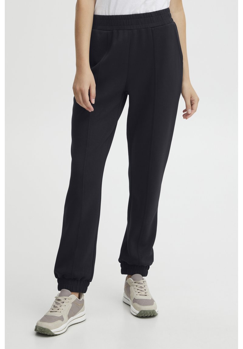 SVART joggebukser med elastisk midjebånd, sidelommer og ribbestrikkede mansjetter. Laget av myk, lett stoff med en glatt tekstur.