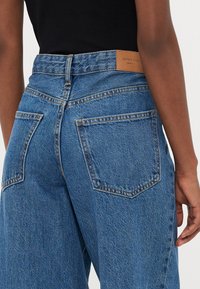 Jeans in denim blu con vita alta, dotati di un'etichetta in pelle marrone sul retro, due tasche posteriori e una vestibilità rilassata.