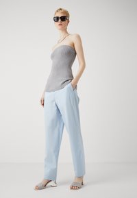 Šedý pletený top bez ramienok, svetlomodré voľné nohavice a strieborné sandále na podpätku s ozdobnými remienkami. Modelka má na sebe čierne slnečné okuliare.