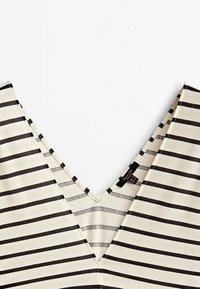 Tissu blanc avec des rayures horizontales noires uniformément espacées et un col en V profond montrant une étiquette noire de vêtement à l'intérieur.