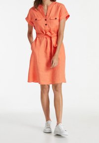 Vestido de lino naranja de manga corta con cuello, botonera en la parte delantera, dos bolsillos en el pecho y cintura ajustada, combinado con zapatillas blancas.