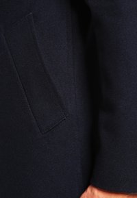 Cappotto in lana blu navy con tessuto testurizzato, dettagli delle tasche laterali, cuciture pulite e una vestibilità sartoriale per un aspetto elegante.