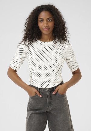 Kortärmad, witte blouse met polka dots en een ronde hals, gecombineerd met hoogwaisted donkergrijze spijkerbroek. De textuur lijkt glad en casual.