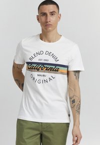Hvit bomull t-skjorte med grafisk trykk som har teksten "Blend Denim California Malibu Original" i svart, samt flerfargede striper over brystet.