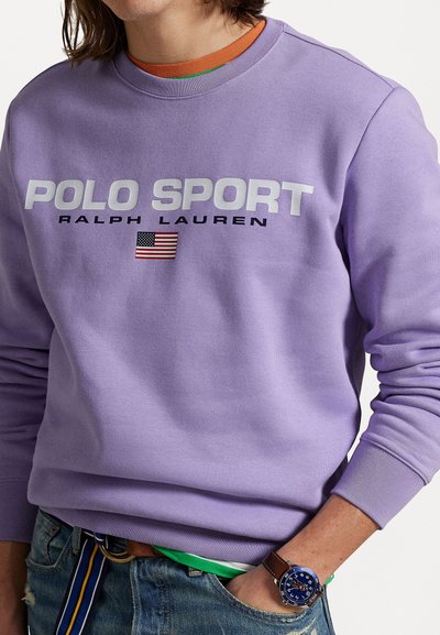 Fialová mikina s veľkým bielym nápisom "POLO SPORT" a "RALPH LAUREN" v čiernej farbe. Obsahuje detail americkej vlajky. Vyrobená z bavlny.