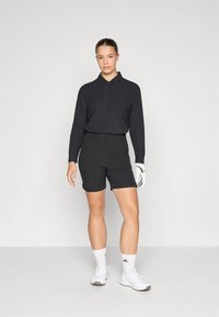 Black long-sleeve polo shirt with three buttons, paired with black shorts. White athletic shoes and golf glove. Simple design and materials.