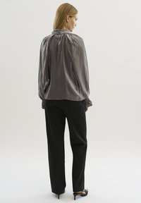 Zilveren satijnen blouse met een hoge kraag en een keyhole-detail aan de achterkant. Gecombineerd met zwarte broek en hoge sandalen. Soepele textuur, losse pasvorm.
